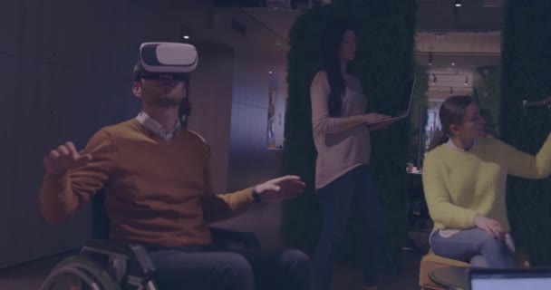 Tekerlekli sandalyedeki engelli işadamı, sanal gerçeklik gözlüğü ve insansız hava aracı simülasyonu kullanarak takım toplantısı için modern açık alan ofisinde çalışıyor. — Stok video