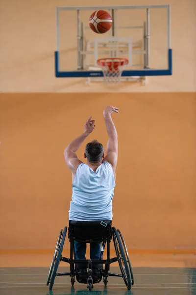 Uma guerra inválida em uma cadeira de rodas treina com uma bola em um clube de basquete em treinamento com equipamentos esportivos profissionais para deficientes. o conceito de esporte para pessoas com deficiência — Fotografia de Stock