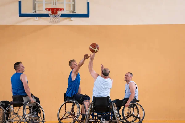 Deficientes veteranos de guerra mista raça opondo equipes de basquete em cadeiras de rodas fotografados em ação enquanto joga um jogo importante em um salão moderno. — Fotografia de Stock