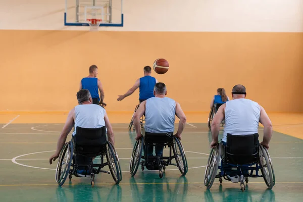 Deficientes veteranos de guerra mista raça opondo equipes de basquete em cadeiras de rodas fotografados em ação enquanto joga um jogo importante em um salão moderno. — Fotografia de Stock