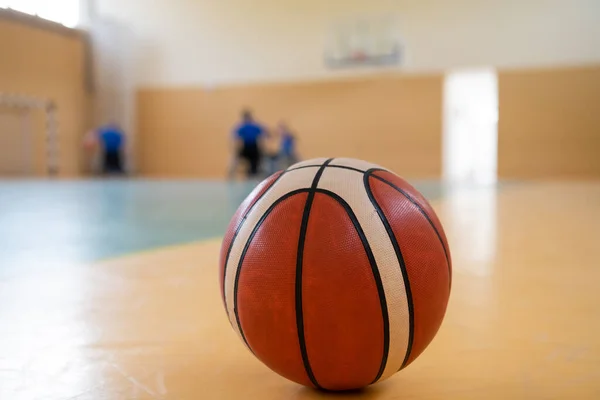 Gros plan photo d'un ballon de basket sur le terrain, en arrière-plan une équipe sportive de personnes handicapées se préparant pour un match — Photo