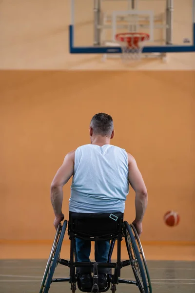 Uma guerra inválida em uma cadeira de rodas treina com uma bola em um clube de basquete em treinamento com equipamentos esportivos profissionais para deficientes. o conceito de esporte para pessoas com deficiência — Fotografia de Stock