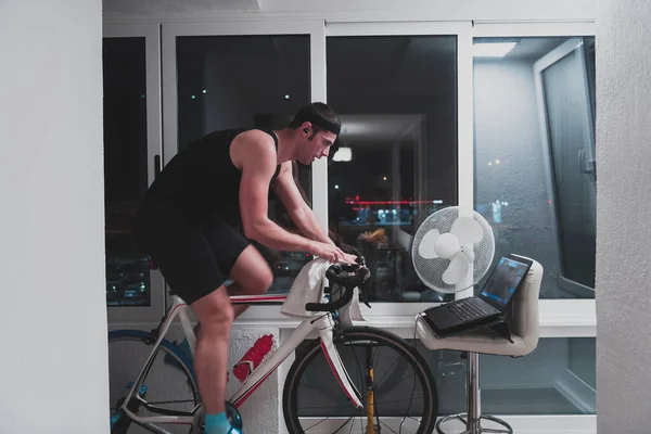 Man kerékpározás a gép tréner ő gyakorolja az otthoni éjjel játszik online bike racing játék — Stock Fotó
