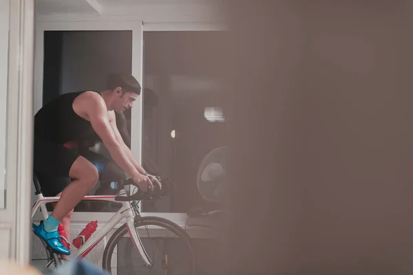 Mann radelt auf dem Maschinentrainer, den er nachts zu Hause trainiert und spielt Online-Radrennspiel — Stockfoto