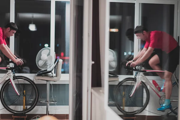 Man fietsen op de machine trainer hij oefent in het huis 's nachts spelen online fiets race spel — Stockfoto
