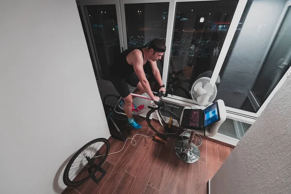 Ο άνθρωπος ποδηλασία για τον εκπαιδευτή μηχανή που ασκεί στο σπίτι το βράδυ παίζοντας online ποδήλατο αγωνιστικά παιχνίδι — Φωτογραφία Αρχείου
