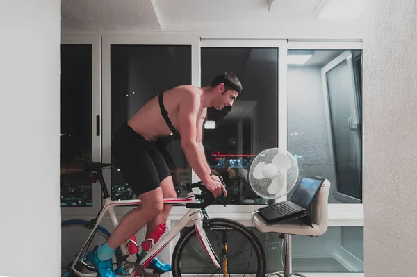 Man cycling on the machine trainer he is exercising in the home at night playing online bike racing game — Stock Photo, Image