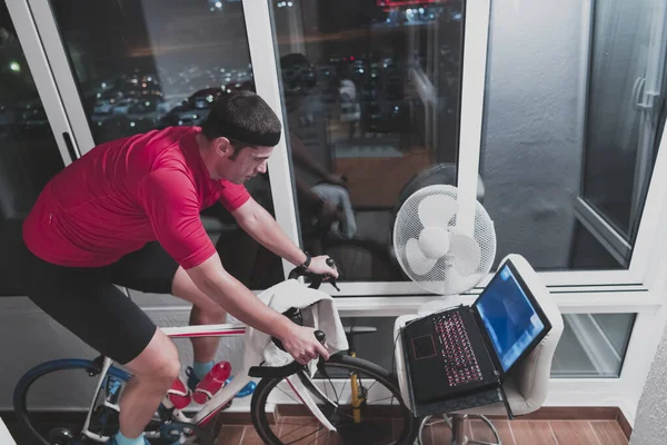 Man fietsen op de machine trainer hij oefent in het huis 's nachts spelen online fiets race spel — Stockfoto