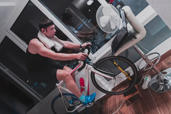 Man fietsen op de machine trainer hij oefent in het huis 's nachts spelen online fiets race spel — Stockfoto