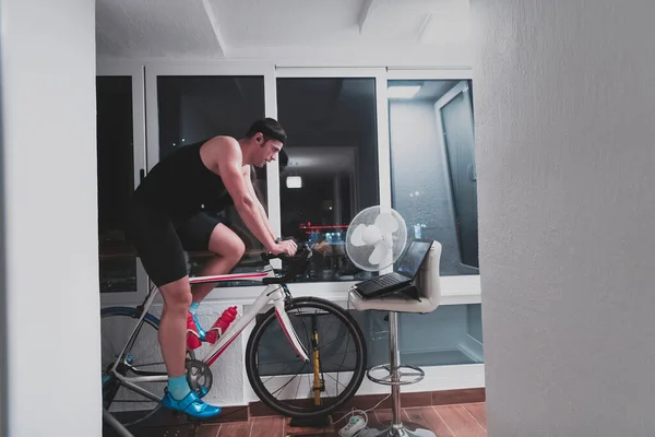 Man cycling on the machine trainer he is exercising in the home at night playing online bike racing game — Stock Photo, Image