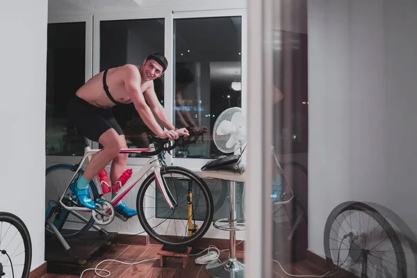 Ο άνθρωπος ποδηλασία για τον εκπαιδευτή μηχανή που ασκεί στο σπίτι το βράδυ παίζοντας online ποδήλατο αγωνιστικά παιχνίδι — Φωτογραφία Αρχείου