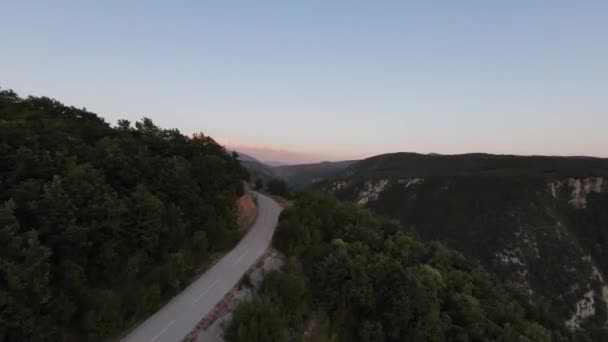 Aerial cineatic shot high speed sport fpv drone flying over natural mountain cliff canyon country road umgeben von atemberaubender Natur felsiges Gelände mit grüner Vegetation und Wald bei Sonnenuntergang. — Stockvideo