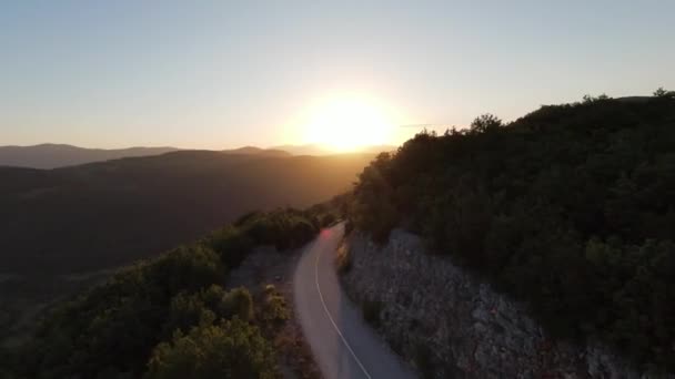緑の植生と日没の森と素晴らしい自然の岩の地形を囲まれた自然の山の崖の峡谷の国の道路上を飛んで空中の映画撮影高速スポーツfpvドローン. — ストック動画