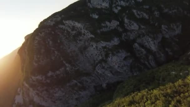 Flygfoto foto hög hastighet sport fpv drönare flyger över naturliga berg klippa kanjon land väg omgiven Fantastisk natur stenig terräng med grön vegetation och skog på solnedgången. — Stockvideo