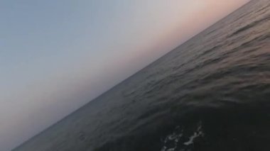 FPV insansız hava aracı okyanus kıyısında hızla uçarken arka planda mavi okyanus sularına ve mavi gökyüzüne kısa bir bakış attı.. 