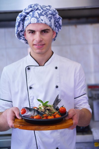 Handsome chef dressed in white uniform holding fish meal