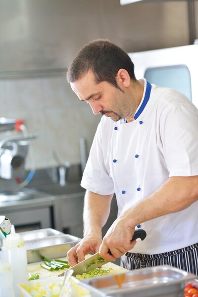 Handsome chef dressed in white uniform cooking at kitchen