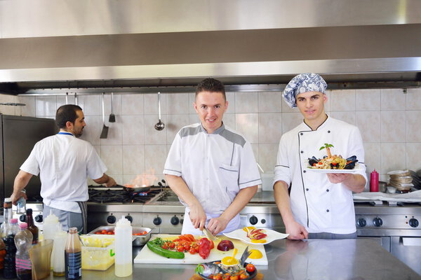 Group of Handsome chefs dressed in white uniform decorating pasta salad and seafood fish in modern kitchen