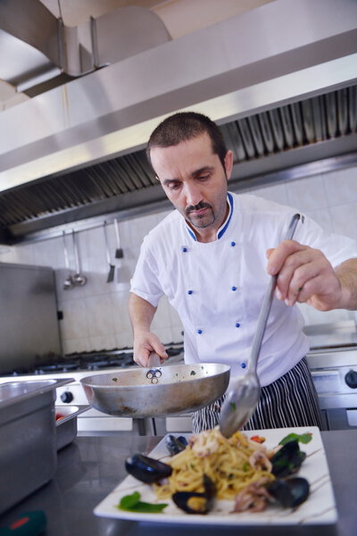 Handsome chef dressed in white uniform decorating seafood pasta salad in modern kitchen