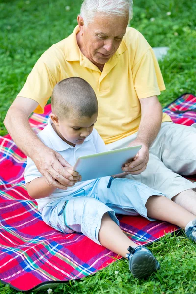 Grandfather and child in park using tablet — Stock Photo, Image