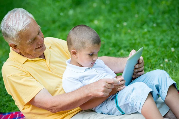 Grandfather and child in park using tablet — Stock Photo, Image