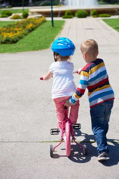 เด็กชายและเด็กผู้หญิงในสวนเรียนรู้ที่จะขี่จักรยาน — ภาพถ่ายสต็อก