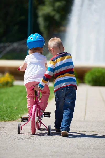 Boy and girl in park learning to ride a bike — Stock Photo, Image