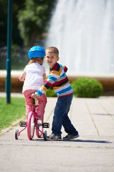 Boy and girl in park learning to ride a bike — Stock Photo, Image