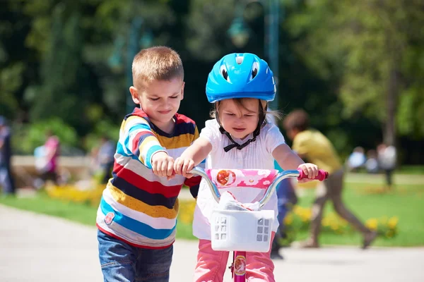 Boy and girl in park learning to ride a bike — Stock Photo, Image