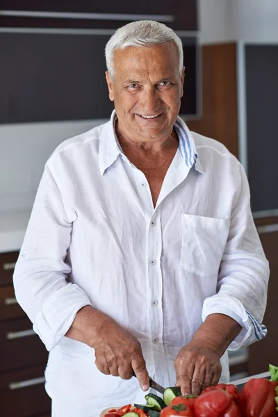 Senior man cooking at home preparing salad — Stock Photo, Image