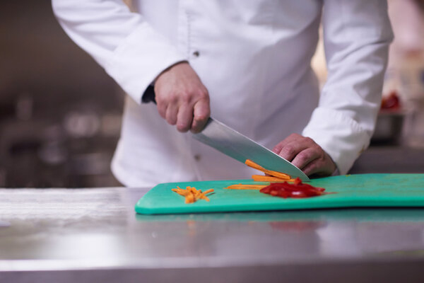 Chef slicing vegetables with knife, preparing food in hotel kitchen