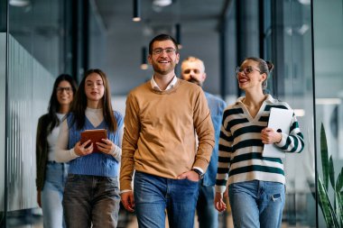 Bir grup genç iş adamı modern ofis koridorunda birlikte yürüyor, gülümsüyor ve iş tartışıyorlar. Güven, takım çalışması, liderlik ve pozitif işyeri kültürü kavramı