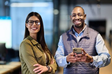 Modern bir ofiste birlikte duran iki neşeli iş arkadaşı, güvenle gülümsüyor ve profesyonel bir iş ortamında pozitif takım çalışması, başarı ve dostça bir işbirliği sergiliyorlar.