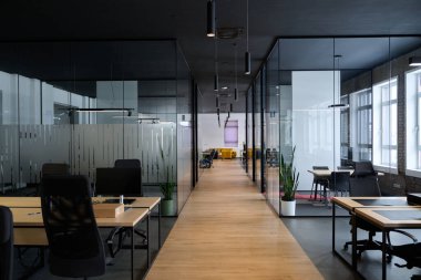 Minimalist tasarım, siyah sandalyeler, ahşap masalar ve cam bölümler ile çağdaş açık uzay ofis iç mimarisi profesyonel bir şirket çalışma ortamını temsil etmektedir.