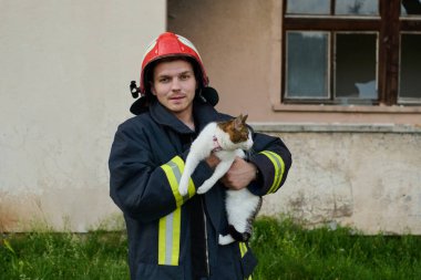 Bir itfaiyeci yanan bir binadan kurtarılmış bir kediyi tutuyor. Kahraman üniforma ve kask giyiyor, şehir ortamında cesaret ve şefkat gösteriyor. Bu resim kurtarılmayı temsil ediyor