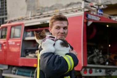 Bir itfaiyeci kurtarılmış bir kediyi itfaiye arabasının önünde tutuyor. Bu görüntü cesaret, şefkat ve itfaiyecilerin hem insan hem de hayvan hayatları kurtarmada oynadıkları önemli rolü temsil ediyor. Mükemmel.