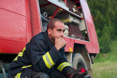 Üniformalı bir itfaiyeci, itfaiye aracına binip kurtarma operasyonlarını dikkatlice düşünür. Bu görüntü, doğal ortamdaki acil durum hizmetleri, yangın güvenliği, eğitim ve toplum desteğini temsil etmektedir.