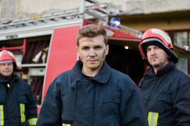 Profesyonel itfaiyeciler itfaiye arabasının yanında durur, harekete geçmeye hazırdırlar. Bu görüntü takım çalışmasını, acil servisleri ve itfaiye teşkilatlarının ithafını temsil ediyor. Resmetmek için ideal