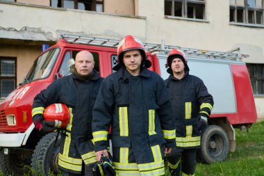 İtfaiye arabasının önünde poz veren üniformalı ve kasklı bir grup itfaiyeci. Bu resim acil durum hizmetleri, kurtarma operasyonları, yangın güvenliği ve cesaret için uygundur.