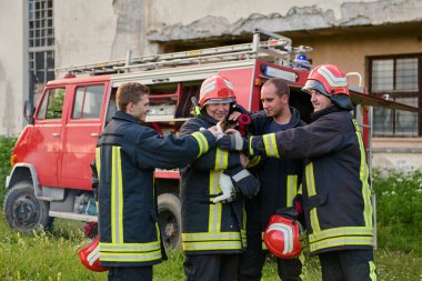 İtfaiyecilerden oluşan bir ekip bir kediyi yangından kurtarıyor. İtfaiyeciler kedi yavrusunu tutuyor, takım çalışması ve şefkat gösteriyorlar. İtfaiye aracı arka planda, acil durum görüntüsü veriyor..