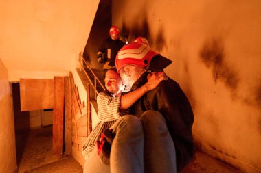 Kurtarılmış bir kadını acil durum tahliyesi sırasında yanan merdivenlerden aşağı taşıyan cesur itfaiyeci, kahramanlığı ve tehlikeli durumlarda hayat kurtarmayı sembolize ediyor.