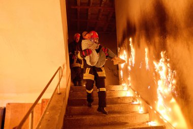 Kurtarılmış bir kadını acil durum tahliyesi sırasında yanan merdivenlerden aşağı taşıyan cesur itfaiyeci, kahramanlığı ve tehlikeli durumlarda hayat kurtarmayı sembolize ediyor.