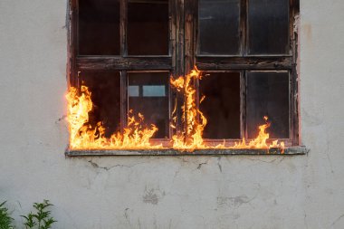 Alevlerle kaplanmış eski bir ahşap pencerenin dramatik bir görüntüsü. Tehlike, yıkım, acil durumlar ve yangının mülkiyet üzerindeki etkisini göstermek için mükemmel..