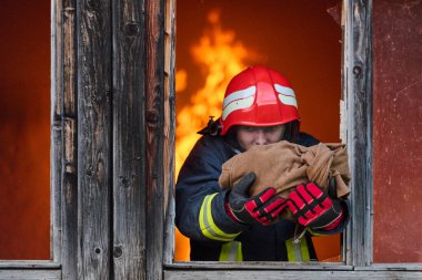 Bir itfaiyeci yanan bir binadan bir bebeği kurtarıyor. İtfaiyeci harekete geçti, çocuğu acil durumdan kurtardı. Bu görüntü cesaret ve kurtarma temalarını göstermek için kullanılabilir.
