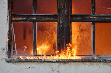 Yanan bir binayı ve yangın tehlikesini gösteren bir pencere alevler içinde kaldı. Bu görüntü yangın güvenliğini, acil durumları ve yangının yol açtığı yıkımı göstermek için kullanılabilir.