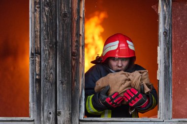 Bir itfaiyeci yanan bir binadan bir bebeği kurtarıyor. İtfaiyeci harekete geçti, çocuğu acil durumdan kurtardı. Bu görüntü cesaret ve kurtarma temalarını göstermek için kullanılabilir.