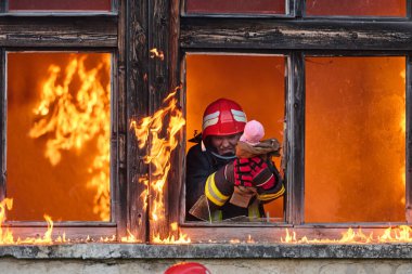 Bir itfaiyeci yanan bir binadan bir bebeği kurtarıyor. İtfaiyeci harekete geçti, çocuğu acil durumdan kurtardı. Bu görüntü cesaret ve kurtarma temalarını göstermek için kullanılabilir.