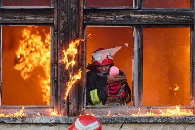 Bir itfaiyeci yanan bir binadan bir bebeği kurtarıyor. İtfaiyeci harekete geçti, çocuğu acil durumdan kurtardı. Bu görüntü cesaret ve kurtarma temalarını göstermek için kullanılabilir.