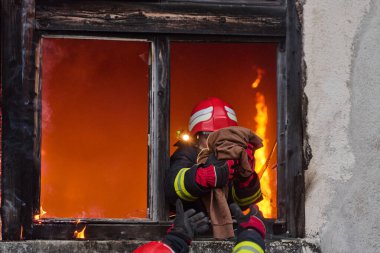 İtfaiyeciler yanan bir binada alevlerle savaşıyor. Bu görüntü itfaiyecilerin karşılaştığı tehlikeleri ve zorlukları ve acil durum müdahalesinin önemini göstermek için kullanılabilir.