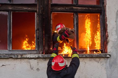 İtfaiyeciler yanan bir binada alevlerle savaşıyor. Bu görüntü itfaiyecilerin karşılaştığı tehlikeleri ve zorlukları ve acil durum müdahalesinin önemini göstermek için kullanılabilir.